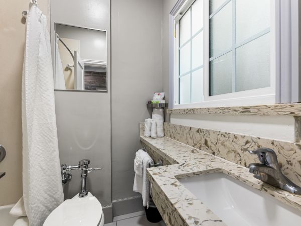 A compact, modern bathroom with a marble countertop, dual sink, wall mirror, shower with curtain, and a frosted window; clean and bright.