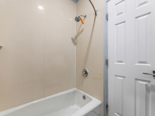 A simple bathroom with a white bathtub, beige tiled walls, a wall-mounted showerhead, and a closed white paneled door.