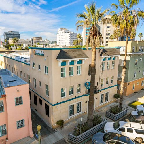 Colorful mid-century buildings on a sunny street with palm trees and parked cars, creating a coastal downtown vibe.