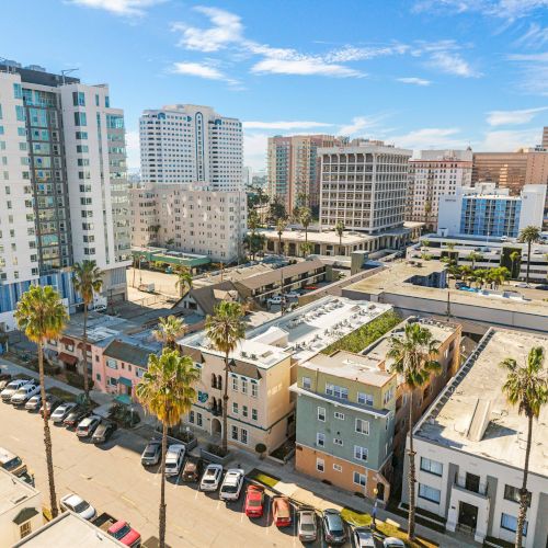 A sunny urban vista with mid-rise buildings, palm trees lining the streets, and a mix of residential and commercial structures in a coastal city.