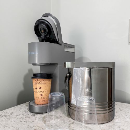 A sleek coffee machine brewing a cup of latte on a marble counter, with a frothing pitcher nearby and a wall switch in the background.
