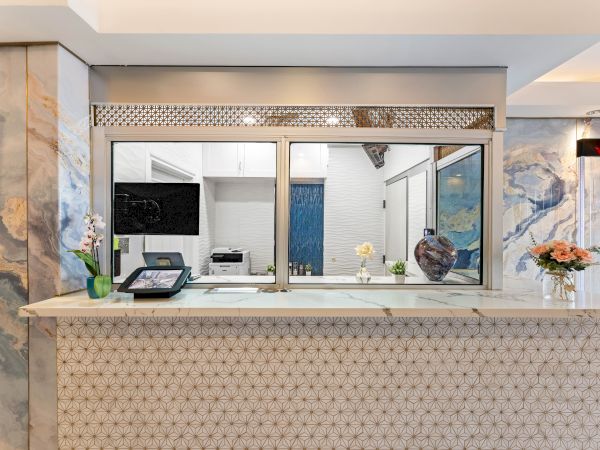 A hotel reception desk with a window to the inside, flowers, and a small vase on the counter.