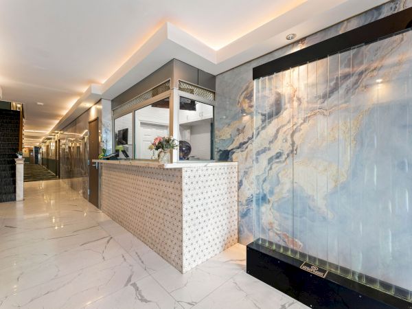 A modern hotel lobby with a marble floor, a long reception desk, subtle lighting, and a large abstract wall feature.