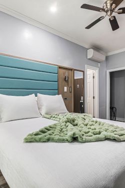 A modern hotel room with a large bed, teal tufted headboard, ceiling fan, desk, seating area, and gray tones. End.