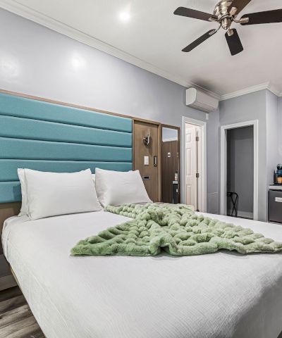 A modern hotel room with a large bed, teal tufted headboard, ceiling fan, desk, seating area, and gray tones. End.