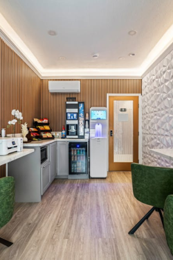 A modern, stylish lounge with a wooden slat wall, white geometric accent wall, green chairs, a coffee bar area, small plants, and a bright, inviting vibe.