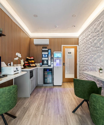 A modern, stylish lounge with a wooden slat wall, white geometric accent wall, green chairs, a coffee bar area, small plants, and a bright, inviting vibe.