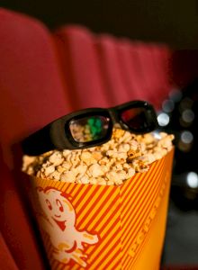 A cupcake with white frosting, sprinkles, and colorful toppings topped with a cherry.