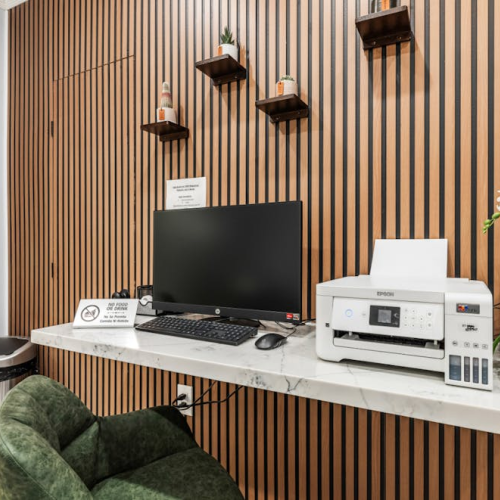 A modern office reception area with a marble desk, computer, printer, green chair, wooden slat wall, and potted orchid accents.